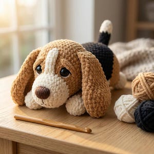 Puede incluir: Un juguete de peluche tipo beagle tejido a ganchillo con hilo color canela, blanco y negro, con grandes ojos oscuros y nariz marrón. El animal de peluche tiene orejas largas y caídas y una cola pequeña, junto a un ganchillo de madera y tres ovillos.