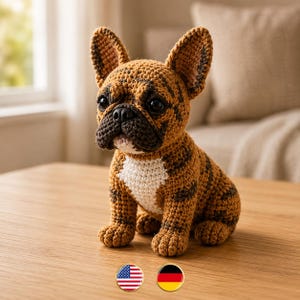 Può includere: Una statuetta di bulldog francese all'uncinetto con un motivo in filato tigrato marrone e nero, grandi orecchie dritte, un muso marrone scuro e una macchia bianca sul petto. Il giocattolo ha occhi in plastica nera e un naso nero.