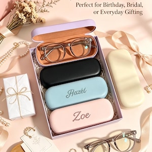 May include: A rectangular lavender gift box containing four hard-shell glasses cases in lavender, black, light blue, and light pink. The light blue case features the name Hazel and the light pink case features the name Zoe in rhinestones.
