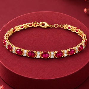 Pode incluir: Uma pulseira de tom dourado com um padrão repetitivo de pedras vermelhas de corte oval alternadas com pequenas pedras redondas transparentes. A peça de joalharia inclui um fecho de lagosta seguro e uma corrente extensora de elos.