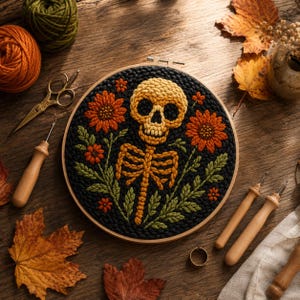 May include: A circular embroidery hoop containing a punch needle design of a yellow skull and ribcage surrounded by orange flowers and green leaves on a black background, accompanied by wooden tools, yarn, and autumn leaves.