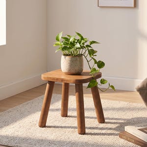 Könnte beinhalten: Ein kleiner, quadratischer Beistelltisch aus Holz mit vier abgerundeten Beinen trägt einen gesprenkelten, hellen Keramiktopf mit einer hängenden grünen Efeutute. Der Tisch hat eine glatte Oberfläche aus Naturholz und eine stabile Bauweise.