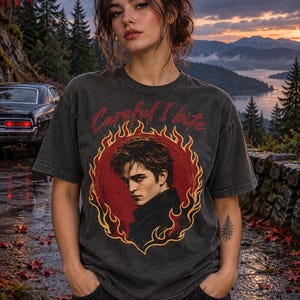 Könnte beinhalten: Ein anthrazitfarbenes Kurzarm-T-Shirt mit einem Grafikdruck einer Person in einem gelben und orangefarbenen Flammenkreis. Der Text "Careful I bite" ist in Rot über dem kreisförmigen Design gedruckt. Das Shirt hat einen Rundhalsausschnitt.