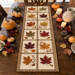 May include: A rectangular fabric table runner featuring a grid of twelve square panels, each decorated with embroidered autumn maple leaves in shades of red, orange, yellow, and green, accented with small pumpkins, acorns, and berries.