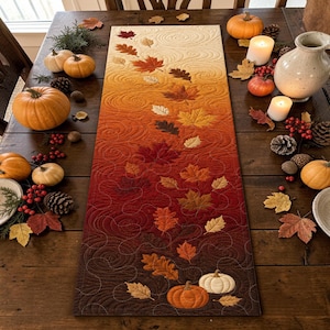 May include: A rectangular fabric table runner featuring a gradient color transition from cream to deep burgundy. The surface is decorated with quilted swirling patterns and appliqued autumn leaves in shades of orange, red, and brown, with two pumpkins.