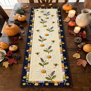 May include: A rectangular quilted table runner featuring a cream-colored center panel with an embroidered pattern of white daisies, purple lavender sprigs, and small bees. The runner is bordered by a dark blue fabric with yellow floral accents.
