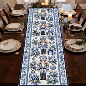 May include: A rectangular table runner featuring a repeating pattern of blue and white nutcrackers, ornate holiday ornaments, gift boxes, and evergreen branches on a cream background, framed by a blue floral border on each side.
