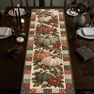 May include: A rectangular quilted table runner featuring a central panel with a repeating pattern of pumpkins, acorns, oak leaves, and red flowers. The border consists of a patchwork design in shades of green, red, and cream with a stitched texture.