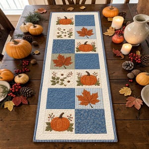 May include: A rectangular quilted table runner featuring a patchwork design of blue fabric squares and cream squares decorated with embroidered orange pumpkins, white flowers, and brown maple leaves, finished with a blue and white checkered border.