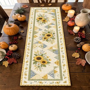 Può includere: Un runner da tavola trapuntato rettangolare con un motivo ripetuto di girasoli gialli e margherite bianche su fondo crema con accenti a quadretti verdi e gialli, bordato da un sottile tralcio di piccoli fiori gialli e foglie verdi.