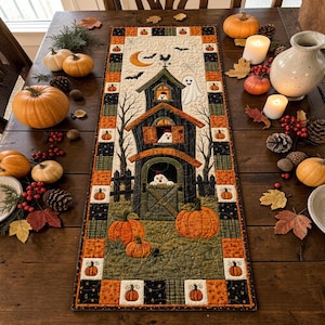 May include: A rectangular quilted table runner featuring a central barn scene with chickens in the windows, a ghost, and a crescent moon. The border is composed of alternating orange and black squares decorated with small pumpkin motifs.