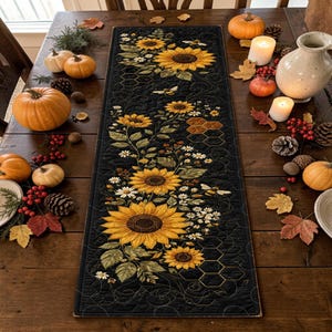 May include: A rectangular quilted table runner featuring a black background with a printed pattern of yellow sunflowers, white daisies, green leaves, honeycombs, and small bees. The fabric has intricate swirling stitch details throughout the surface.