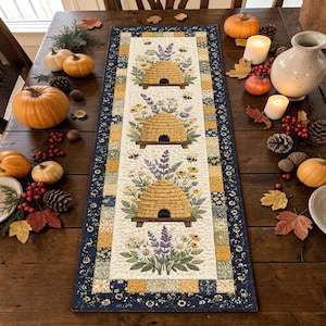 May include: A rectangular fabric table runner featuring a cream-colored center panel with three repeating illustrations of yellow beehives surrounded by lavender and daisies, framed by a dark blue border with a yellow and green patchwork pattern.