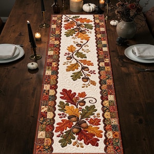 Puede incluir: Un camino de mesa rectangular con un panel central de color crema con textura acolchada, decorado con hojas de roble, bellotas y bayas de otoño. El borde consiste en un patrón de patchwork de cuadrados en tonos marrones, naranjas y verdes.