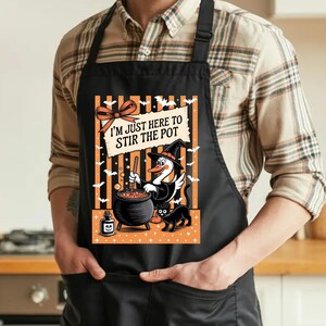 May include: A black apron featuring a graphic of a duck wearing a witch hat, stirring a cauldron with a black cat nearby. The design includes orange and black stripes, bats, and the text I'M JUST HERE TO STIR THE POT with a small orange bow.