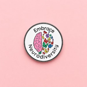 May include: A circular enamel pin featuring a white background and a black rim. The design displays a pink brain on the left half and a cluster of multi-coloured butterflies on the right. The text Embrace Neurodiversity is printed in black around the edge.