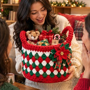 Peut inclure: Un panier rond au crochet avec un motif en losanges rouge, blanc et vert. Le panier possède deux anses robustes et est orné sur le devant d'une grande fleur de poinsettia rouge au crochet, de feuilles vertes et d'un nœud en ruban écossais.