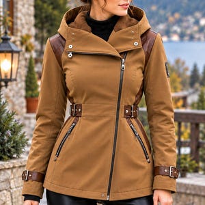 May include: A tan hooded jacket featuring a diagonal front zipper, dark brown leather-like shoulder panels, and adjustable buckled straps at the waist and cuffs. The jacket includes two zippered side pockets and a high collar with a black inner layer.