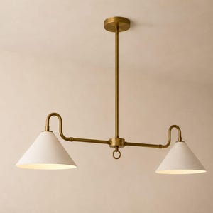 May include: A ceiling-mounted light fitting featuring a central brass rod and a horizontal arm with two curved ends. Each end supports a white conical shade pointing downwards. The metal finish is a matte brass, and a small ring hangs from the centre.