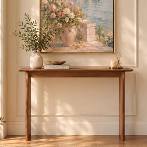 May include: A rectangular framed oil painting depicting a coastal Mediterranean village with stone buildings, cypress trees, and a floral arrangement in a vase on a terrace overlooking a calm blue sea under a soft, light-filled sky.