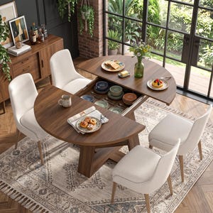 May include: A round walnut-finished dining table with a split top that slides open to reveal a hidden storage compartment containing various ceramic bowls and plates, surrounded by four off-white upholstered chairs on a patterned rug.