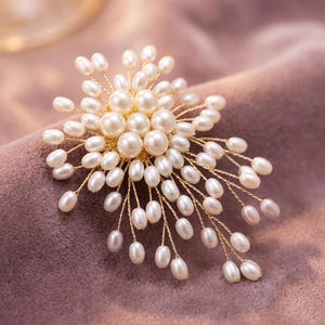May include: A brooch featuring a cluster of small, white, oval-shaped freshwater pearls attached to thin, gold-toned wire stems. The pearls are arranged in a radiating, spray-like pattern, with larger round pearls at the center and smaller pearls extending outward on individual wire branches.