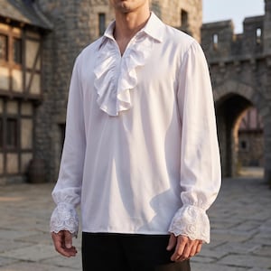 Peut inclure: Une chemise blanche à manches longues dotée d'un jabot à volants proéminent sur le devant, d'un col classique et de larges poignets ornés d'une broderie en dentelle florale blanche complexe. Le vêtement présente une coupe ample et des manches longues.