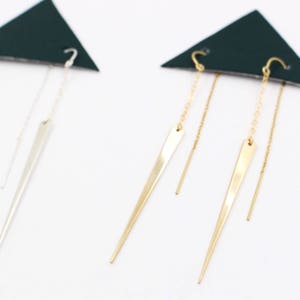 May include: Two pairs of dangle earrings with a long, pointed, silver and gold pendant. Each earring has a chain and a thin, straight wire hanging from the pendant.