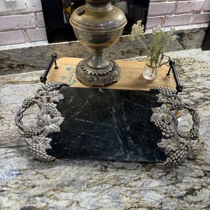 May include: A rectangular serving tray featuring a dark green marble center panel. The tray has two ornate silver-toned metal handles on each side, each decorated with detailed relief carvings of grape clusters and vine leaves.