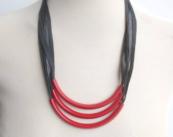 May include: A layered necklace with a black leather cord and three red, curved, plastic pieces.
