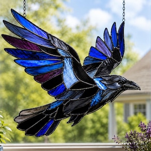 Könnte beinhalten: Ein Buntglas-Sonnenfänger in Form eines fliegenden Vogels mit ausgebreiteten Flügeln. Das Stück besteht aus einzelnen Glassegmenten in den Farben Tiefblau, Violett und Schwarz, die durch dunkle Metalllötlinien verbunden sind und an Ketten hängen.
