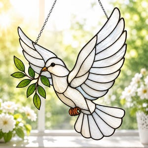 May include: A stained glass suncatcher shaped like a white dove in flight, featuring translucent white wings and body with black lead lines. The dove holds a green glass olive branch in its beak and has orange glass feet, suspended by a metal chain.