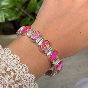 Peut inclure: Un bracelet à maillons en argent composé d'une série de pierres ovales rose irisé avec une texture scintillante aux éclats multicolores. Le bracelet est construit avec des montures en métal argenté poli reliant chaque pierre.