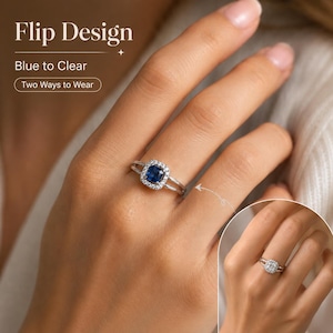Könnte beinhalten: Ein silberfarbener Ring mit einem quadratischen blauen Edelstein, umgeben von einem Kranz aus kleinen klaren Steinen. Der Text Flip Design, Blue to Clear und Two Ways to Wear ist sichtbar. Ein kleiner Einsatz zeigt den Ring mit klarem Stein.