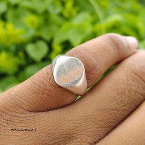 May include: A polished silver signet ring featuring a smooth, rounded, flat face and a solid band. The metal surface has a reflective finish. The text 925SilverBohoArt is printed in the bottom left corner of the image.