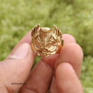 May include: A gold-toned ring featuring a detailed relief of a cobra with flared hood and wings. The design includes intricate scales and textures across the surface of the metal band. The text 925SilverBohoArt is visible in the bottom left corner.