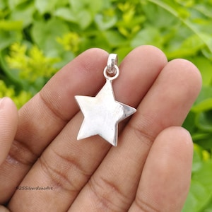 May include: A polished silver star-shaped pendant featuring a smooth, reflective surface and a small circular bail at the top for attachment. The metal charm has five distinct points and includes the text 925SilverBohoArt in the bottom corner.