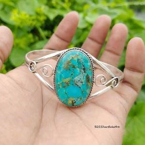 May include: A silver cuff bracelet featuring a large, oval-shaped turquoise stone with brown matrix veining. The metal band displays a twisted rope border around the stone and decorative scrollwork on both sides. The text 925SilverBohoArt is visible.