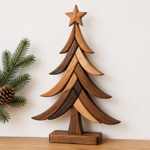 Puede incluir: Una escultura decorativa de árbol de Navidad hecha de segmentos de madera en tonos marrones claros y oscuros. El árbol presenta un diseño de ramas curvas escalonadas y está rematado con una estrella de madera de cinco puntas.