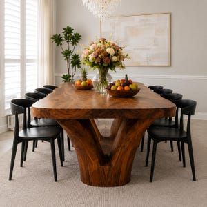 May include: A large dining table with a natural wood grain finish and a thick, organic-shaped slab top supported by a solid, V-shaped pedestal base, surrounded by twelve black chairs with curved backrests and thin, tapered legs.