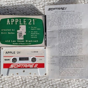 May include: A vintage Apple II (24K) computer game cassette for "Apple 21" Blackjack. The cassette is white with red text and the "Softape" logo. The game description is on a folded paper.