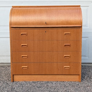 May include: A wooden roll-top desk with four drawers and a curved top. The desk is made of light brown wood and has a keyhole in the center of the roll-top. The drawers have rectangular handles.