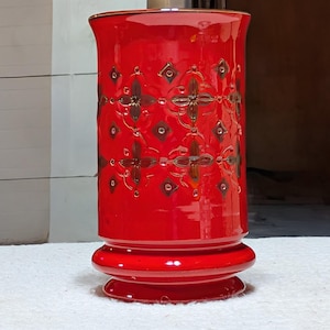 May include: A tall, vibrant red ceramic vase with a flared top and a decorative base. The vase features a repeating pattern of brown floral designs. The vase is approximately 12 inches tall, making it a striking decorative piece.