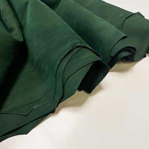 May include: A folded piece of dark forest green leather with a smooth, matte finish. The material is draped in soft, layered waves, showcasing the deep, consistent colour and the natural, flexible texture of the hide as it curves and overlaps.
