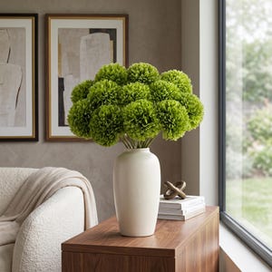 Peut inclure: Un grand vase en céramique blanc cassé, lisse et arrondi, contient un bouquet dense de fleurs artificielles sphériques d'un vert citron vif. Les fleurs présentent une texture en pompon et reposent sur une surface en bois.