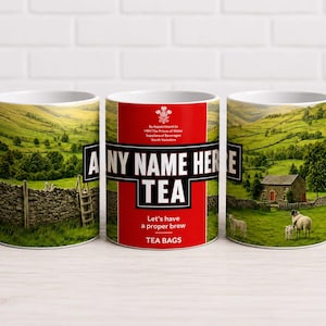 May include: A white ceramic mug featuring a landscape of green hills, a stone wall, and a small house with sheep. The centre panel is red with black text reading ANY NAME HERE TEA, Let's have a proper brew, TEA BAGS, and a white crest logo.