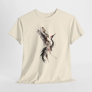 May include: A cream-colored short-sleeve t-shirt featuring a central graphic illustration of a crane with black, white, and red plumage. The design includes flowing ink-style lines and Korean text characters in black ink, centered on the chest.