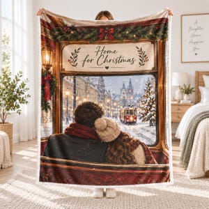 Könnte beinhalten: Eine weiche Wohndecke mit einem Druck von zwei Personen, die aus einem Straßenbahnfenster auf eine verschneite Straße blicken. Der Text Home for Christmas ist oben zentriert und von Tannengirlanden, roten Schleifen und Laternen umrahmt.