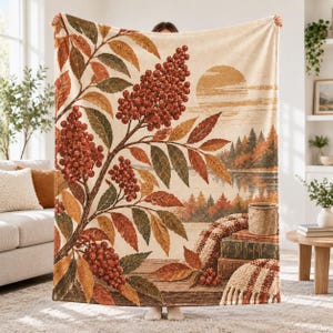 May include: A rectangular throw blanket featuring a printed autumn landscape. The design displays a large branch with red berries and orange, yellow, and green leaves in the foreground, with a lake, forest, and sun in the background.