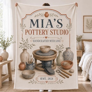 Könnte beinhalten: Eine cremefarbene Fleecedecke mit einem Töpferstudio-Motiv, das den Text "MIA'S POTTERY STUDIO" und "EST. 2021" zeigt. Das Design enthält Illustrationen einer Töpferscheibe, verschiedener Keramikschalen, Vasen und Modellierwerkzeugen.